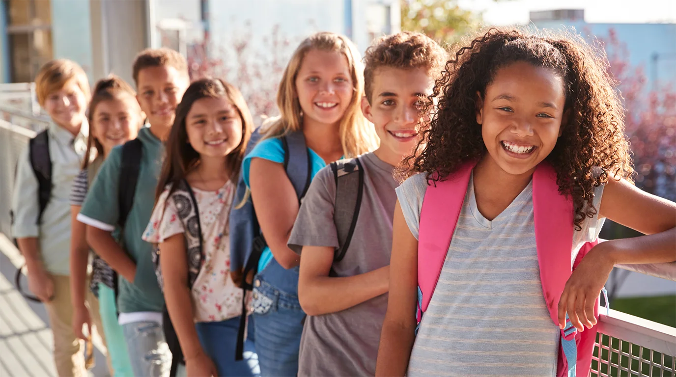 A diverse group of smiling students with backpacks standing together outdoors at school